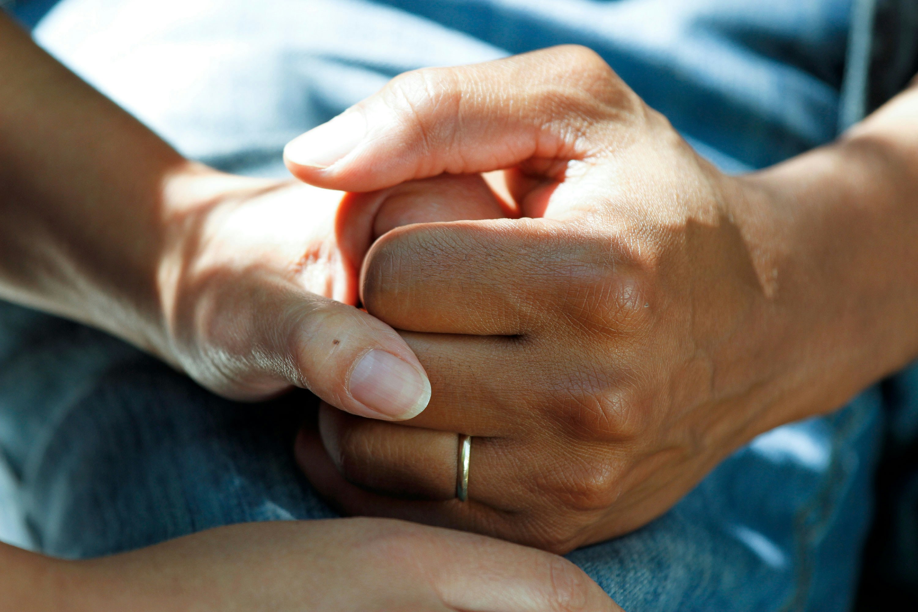 Close-up of two people holding hands, one gently supporting the other, symbolizing care and support.