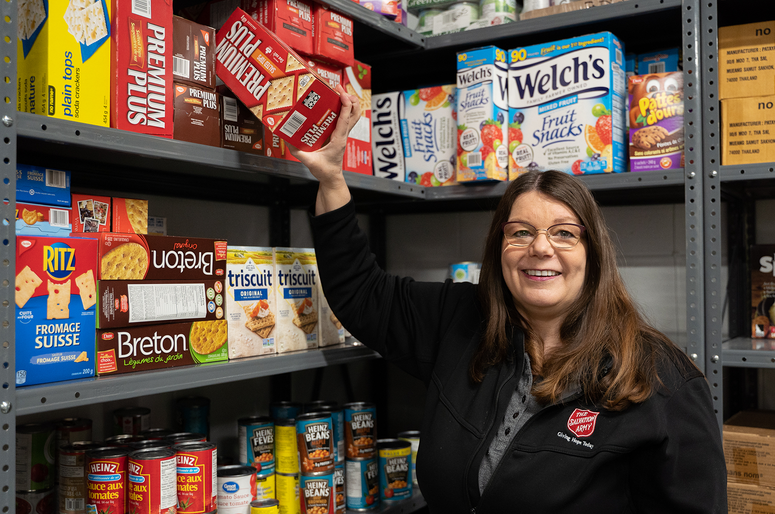 The Salvation Army staff member placing donated food items on a pantry shelf stocked with boxed and canned goods.