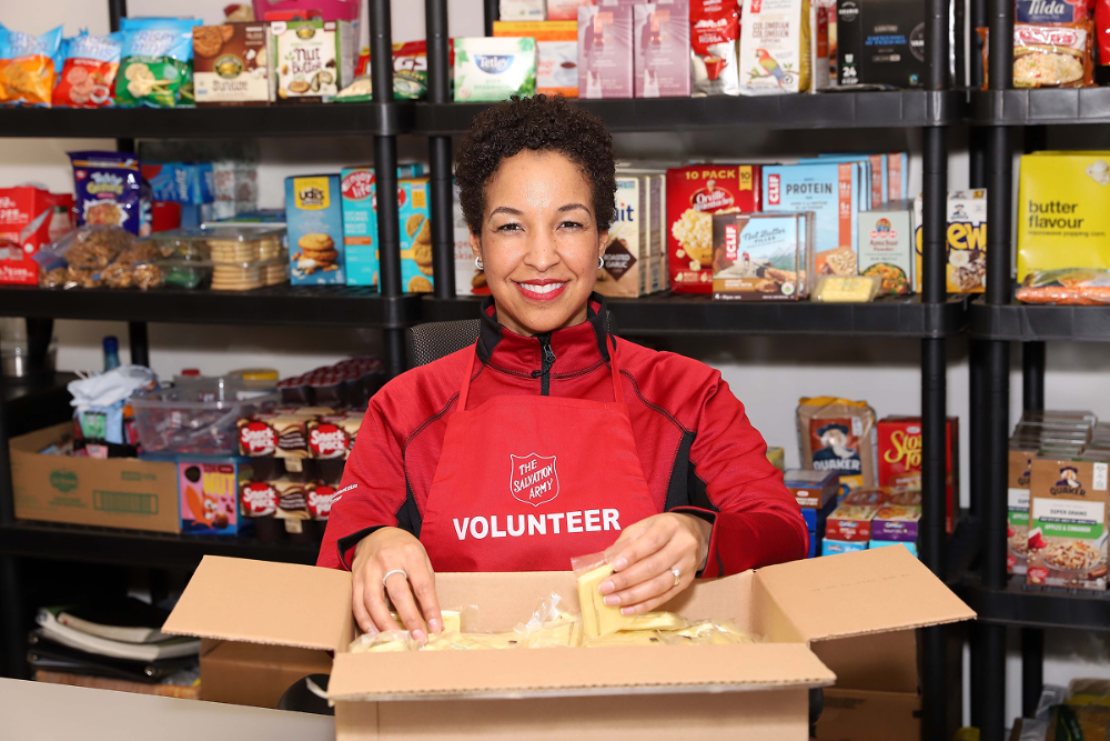 Volunteer wearing a Salvation Army apron packs food items into a box.